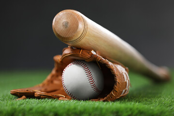 Baseball bat, leather glove and ball on green grass against dark background, closeup