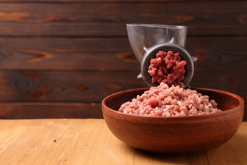 Manual meat grinder with beef mince on wooden table, space for text