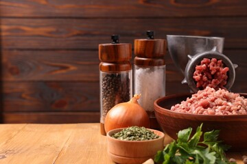 Manual meat grinder with beef mince, spices and parsley on wooden table, space for text