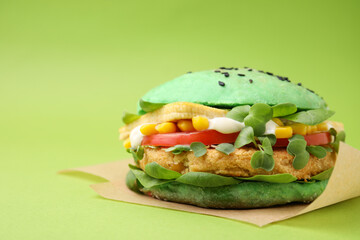 Tasty vegan burger with vegetables, patty and microgreens on green background, closeup. Space for text
