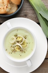 Delicious cream soup with leek and spices in bowl on wooden table, flat lay