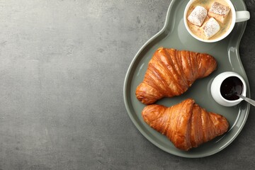 Tasty croissants served with cup of hot drink on grey textured table, top view. Space for text