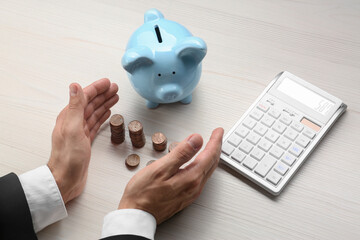Budget planning. Businessman with coins, piggy bank and calculator at light wooden table, closeup