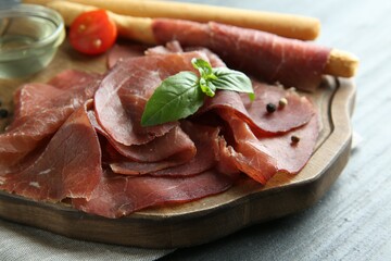 Delicious bresaola and basil leaves on grey textured table, closeup