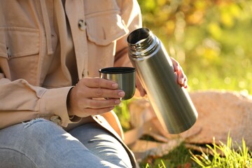 Fototapeta premium Picnic time. Woman with thermos and cup lid on green grass outdoors, closeup
