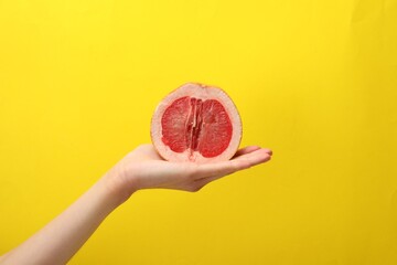 Woman holding half of grapefruit on yellow background, closeup. Sex concept - obrazy, fototapety, plakaty
