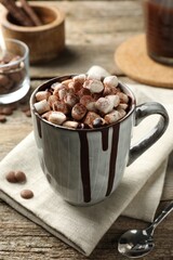 Delicious hot chocolate with marshmallows and cocoa powder in cup on wooden table