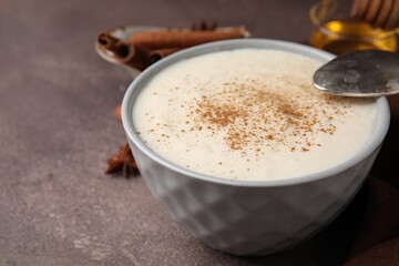 Delicious semolina pudding with cinnamon in bowl and spoon on brown table, closeup. Space for text