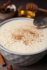 Delicious semolina pudding with cinnamon in bowl and spoon on table, closeup