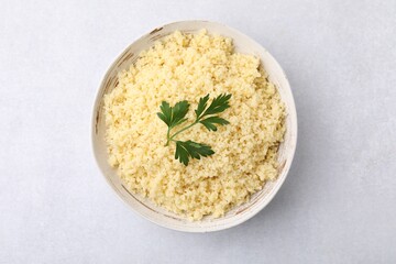 Tasty couscous and fresh parsley in bowl on light grey table, top view