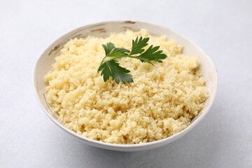 Tasty couscous and fresh parsley in bowl on light grey table, closeup