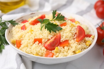 Tasty couscous with parsley, corn and tomatoes in bowl on white table, closeup