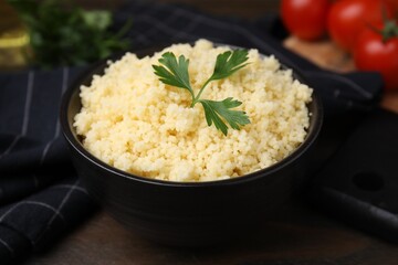 Tasty couscous and fresh parsley in bowl on table, closeup