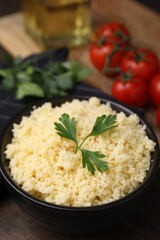 Tasty couscous and fresh parsley in bowl on table, closeup