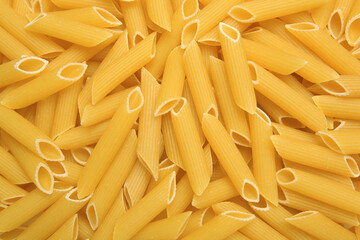Uncooked penne pasta as background, top view