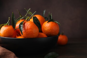 Fresh ripe tangerines with green leaves in bowl on table, closeup. Space for text