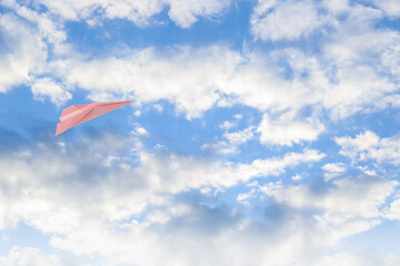 Naklejka na ściany i meble Pink paper plane flying in blue sky with clouds