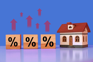 Mortgage rate rising illustrated by upward arrows and percent signs. House model and wooden cubes on table
