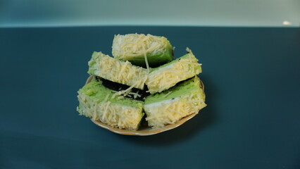 Bolu pandan kukus or chocolate pandan steamed sponge with cheese topping placed on a small plate on a plain background.