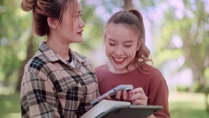 Asian female college student and her friend are reading news on their smartphones and discussing current events in a lush green garden. student life and tech-savvy conversations.