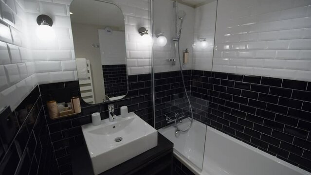 Small black and white bathroom with shower, sink and big mirror on the wall in a hotel room