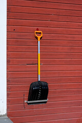 Modern snow shovel hanging on the outside of a rustic wood sided building in the Arctic, prepared...