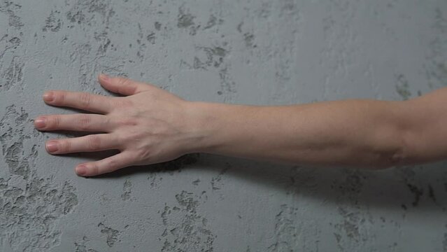 Woman hand palm is touching grey loft concrete  painted hall wall surface at home. House interior modern renovation.