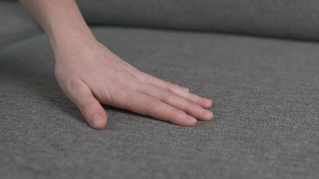 Woman hand palm is touching gray fabric couch surface at furniture shop for home. Modern house interior renovation.