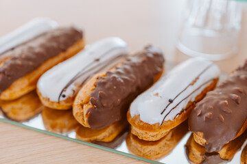 Eclairs with white and chocolate icing are laid out in a row on a mirror surface, display in a store.
