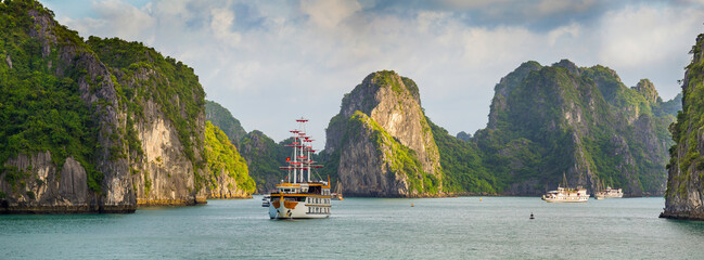 Sailing ship on a calm bay surrounded by high mountain peaks at Ha Long Bay in Vietnam