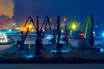  Cargo cranes in selective focus at the cargo port at night in Cherepovets, Russia. Industrial cityscape, transport logistics.
