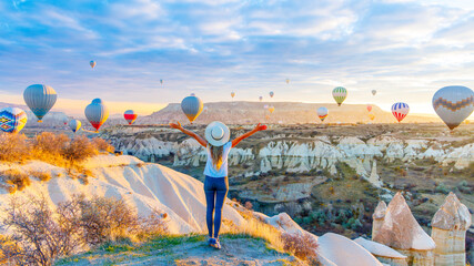 Girl traveler vacation in Turkey- Fairy Cappadocia landscape with flying air balloons at sunrise - obrazy, fototapety, plakaty