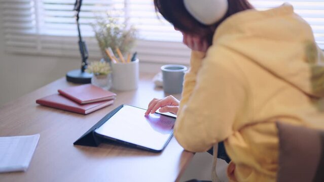 Asian female student attentively reads lesson content or articles online through her tablet at the home desk