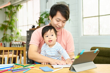 赤ちゃんを抱えて自宅でパソコンを操作する男性