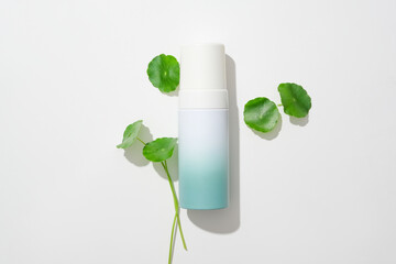 Centella asiatica leaves are decorated around an unbranded cosmetics bottle on a white background. Gotu kola has the ability to stimulate skin cell regeneration.