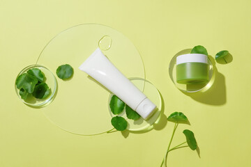 An unlabeled cosmetics set, fresh pennywort and transparent glass platforms are displayed on the background. Scene for vegan cosmetics advertisement.