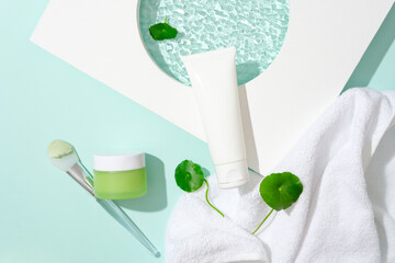 A white tube, a jar of green lotion, a makeup brush, a towel, a podium and pennywort are displayed....