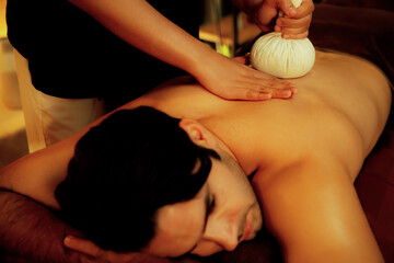 Hot herbal ball spa massage body treatment, masseur gently compresses herb bag on man body....