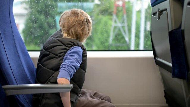 Cute preteen boy is traveling in a local train carriage or by railroad while it rain outside. Portrait of child passenger.