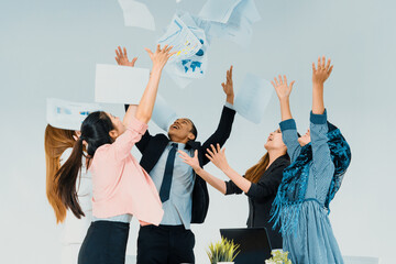 Smiling business people having fun by throwing papers in the air celebrating business success in...