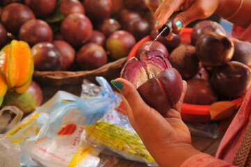 female fruits vendor hands peeling a caimito (purple star apple) with a knife.