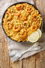Healthy seafood dish Risotto with shrimp, lemon and fresh herbs closeup on the plate on the wooden table. Vertical top view from above