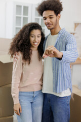 Obraz premium moving to new apartment relocation. happy couple, African American man and woman, hold keys in hands and collect personal belongings in cardboard boxes. purchase of new housing, mortgage.
