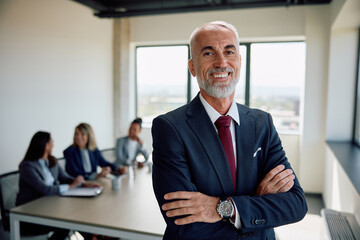 Portrait of happy mature businessman with arms crossed in meeting room looking at camera.