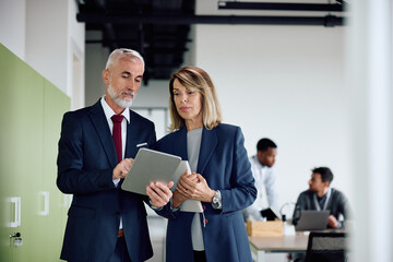 Mature coworkers using digital tablet at corporate office.