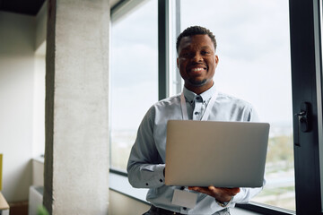 Happy black entrepreneur working on laptop at corporate office and looking at camera.
