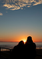 Couple in Love Sitting on Pier Watching Setting Sun, Huntington Beach, California, USA, vertical