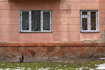 Two white window with bars in a wall covered with plaster
