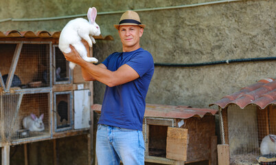 Farmer caucasian rural portrait in countryside with white rabbit in his arms outdoors outside.