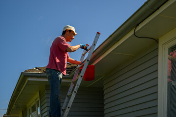 Man standing on the ladder and cleaning the gutter. Home maintenance work. Auckland. © Janice